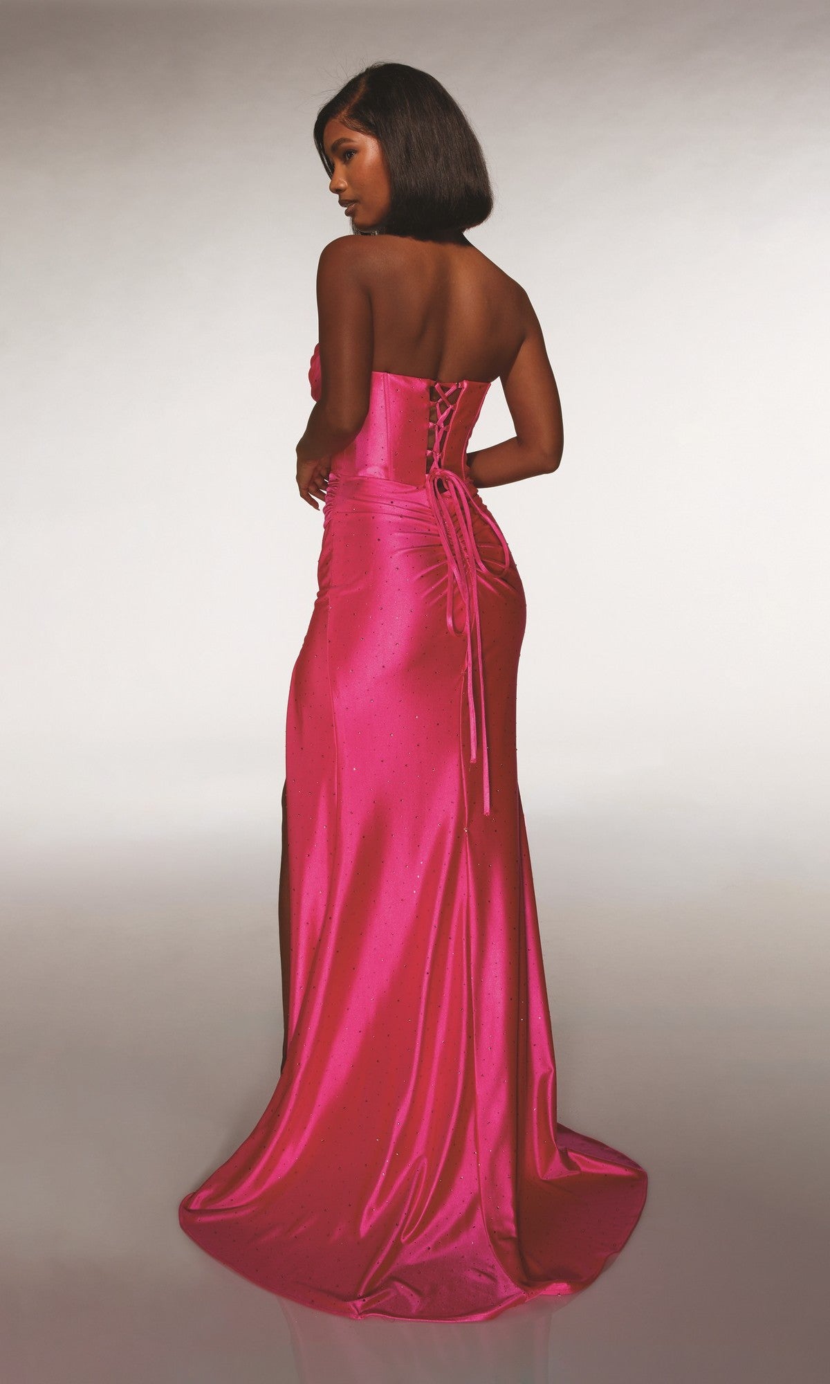 A woman faces away, wearing the Alyce 62099: a strapless, floor-length bright pink prom dress with a corset bodice, lace-up back, and subtle embellishments.